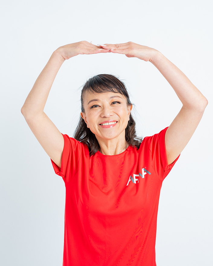 赤いTシャツを着た女性が笑顔で両手を頭の上で丸くしているポーズ