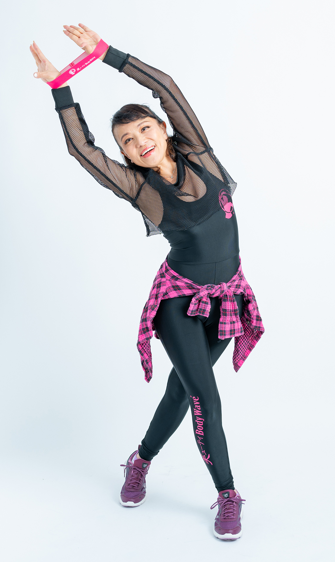 黒いメッシュ衣装とピンクのチェックシャツを着た女性がストレッチポーズをしている様子